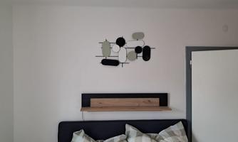 A modern bedroom with an elegant wall decoration above the bed. On the nightstand, there is a wooden board, and the pillows have a checkered pattern.