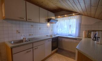 A modern kitchen with bright cabinets and a spacious countertop. The windows bring in plenty of light and offer a view outside.