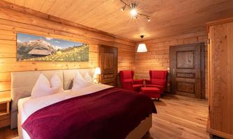 A cozy room with wooden paneling and a large double bed. Red armchairs and a beautiful landscape painting on the wall complement the inviting atmosphere.