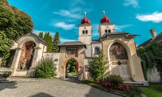 A picturesque residential building with red domes and beautiful frescoes. Surrounded by lush greenery and a paved path.