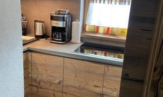 A modern kitchen with wooden cabinets and a coffee machine. Through the window, the landscape with mountains is visible.
