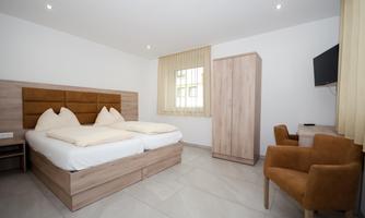 A modern hotel room with two beds, a desk, and a chair. Large windows provide plenty of daylight.