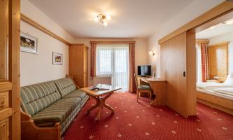 A cozy hotel room with a sofa, a table, and a TV. There are large windows allowing plenty of light and bright colors in the room.