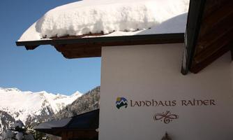 A lovely country house with a snow-covered roof edge. Majestic mountains can be seen in the background.