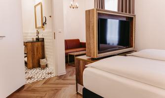 A cozy room with a double bed and a television. In the background, there is a seating area and a visible bathroom.