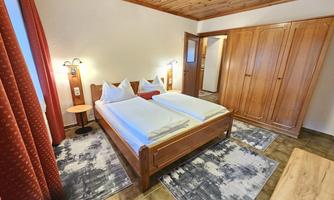 A cozy bedroom with a double bed and wood paneling. The walls are beige, and there is a large wardrobe as well as a table.