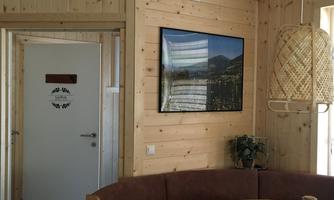 A cozy room with wooden walls and a round table. On the wall hangs a picture of a landscape, and in the background, a door is visible.