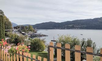 A picturesque view of a tranquil lake, surrounded by hills. Colorful flowers in a garden and a boat dock are visible in the foreground.
