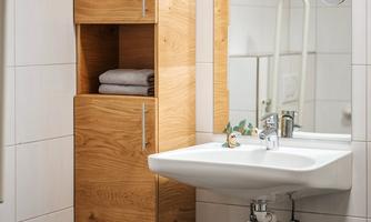 A modern bathroom with a sink and a wooden cabinet. The space has bright tiles and a clear, clean atmosphere.