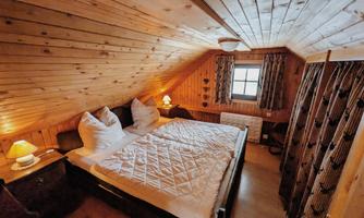 A cozy attic bedroom with wooden ceilings and two beds. Soft pillows and warm lighting create an inviting atmosphere.