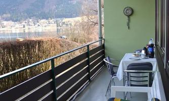 A balcony with a cozy seating area and a table. In the background, mountains and a tranquil landscape can be seen.