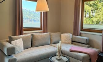 A cozy living room with a bright, modern sofa and a small table. Large windows offer a view of the landscape outside.