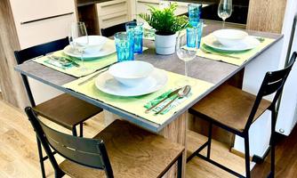 A modern kitchen with a dining area and a table set for two people. The interior design is bright and cheerful with wood and pastel tones.
