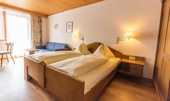 A cozy hotel room with two single beds and a sofa. Large windows provide plenty of daylight.
