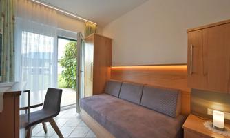 A cozy room with a sofa bed and a small table. Large windows let in plenty of light, and the view into the greenery creates a pleasant atmosphere.