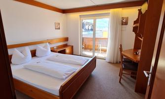 A bright room with two beds and a desk. In the background, there is a balcony with a view.