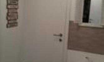 A simple room with a white door and a wall shelf. On the right side, there is a mirror and a small table.