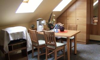 A cozy room with a table and chairs. In the background, there is a cabinet and a coffee machine.