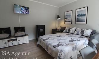 A cozy room with a sofa and a bed, furnished with modern furniture. Pictures of mountains hang on the wall, and a TV is available for entertainment.