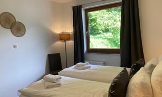 A bright bedroom with two single beds and a large window front. The walls are painted in a calm shade and the room decor is modern and inviting.