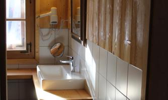 A cozy bathroom with wooden walls and a modern sink. Natural light shines through the window, creating a warm atmosphere.