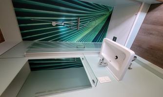 A modern bathroom with a shower and a sink. The wall is decorated with a striking, vibrant design in green and blue.