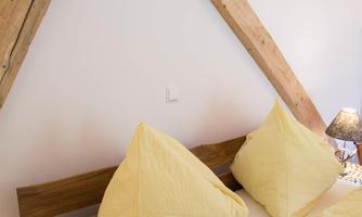 A cozy bedroom with a wooden frame bed and yellow pillows. The walls are decorated with rustic wooden beams.