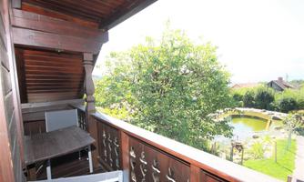 A cozy balcony with a table and chairs. In the background, a green tree and a pond are visible.