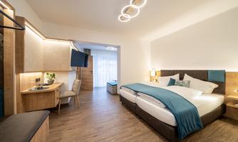 A modern hotel room with a large double bed and hardwood floors. The decor is simple and inviting, with beautiful lighting.