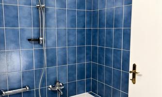 A bathroom with a bathtub and blue tiles. There is a shower with a towel on the bathtub.