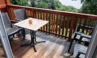 A cozy balcony with a table and chairs. In the background, trees and a green landscape can be seen.