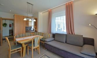 A bright and modern apartment with a cozy seating area. The dining area is furnished with a table and chairs, and the kitchen corner is noticeable.