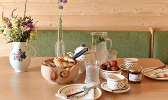 A table set with fresh pastries, strawberries, and a pitcher of water. The background is wooden with a flower vase and a cozy atmosphere.