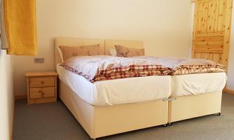 A bedroom with a large, comfortable double bed and a wooden nightstand. The walls are light and the room feels inviting and cozy.