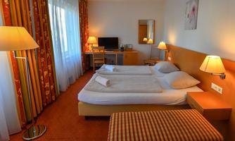 A cozy hotel room with two beds, a desk, and a television. The walls are decorated with colorful curtains and light sources.