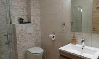 A modern bathroom with bright tiles and a glass shower. There is a sink with a wooden under-sink cabinet and a toilet.