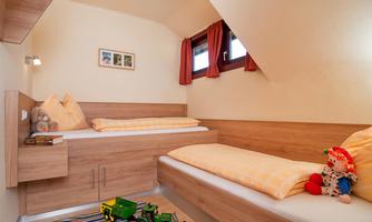 A cozy bedroom with two wooden single beds. On the floor are toys and a small rug.
