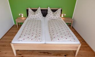 A cozy bedroom with a double bed and two nightstands. The walls are painted green, and the floor is made of wood.