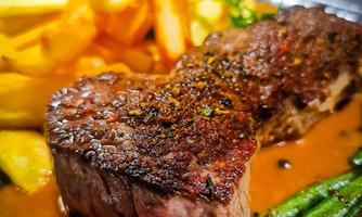 A juicy piece of steak with crispy fries and green beans. The focus is on the flavorful sauce that complements the dish.
