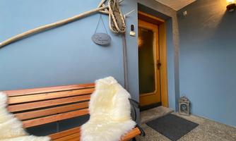 A cozy entrance area with a wooden bench and two fur pillows. The wall is painted in a soft blue, and a flashlight provides warm light.