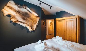 A rustic bedroom with two beds and fresh towels. A fur hangs on the wall, and there is a wooden wardrobe in the background.
