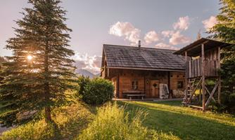 A beautiful wooden house surrounded by trees and meadow. The evening sun is shining, creating a cozy atmosphere.