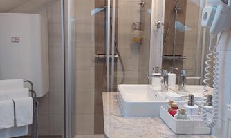A modern bathroom with a glass shower and two sinks. The design is bright and friendly with white and gray tones.