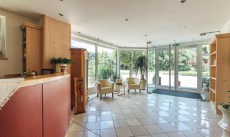 A bright entrance area with large glass fronts and modern furniture. The space has a friendly atmosphere and is well lit.