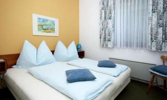 A cozy bedroom with a double bed and bright pillows. The walls are painted in warm colors and there is a window with curtains.