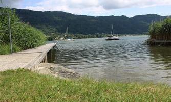 A tranquil lake with a pier and boats. In the background, there are green hills and a partly cloudy sky.