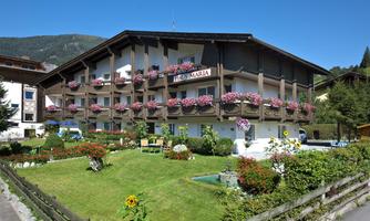 A beautiful house with balconies adorned with flowers. The surroundings are green and well-kept, with a small garden.