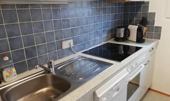 A modern kitchen with a sink, a stovetop, and various kitchen appliances. The walls are tiled with blue tiles.