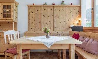 A cozy dining area made of wood with a table and a bench. On the table, there is a small vase with flowers.