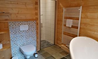 A modern bathroom with wooden paneling. It features a shower, a bathtub, and a toilet.